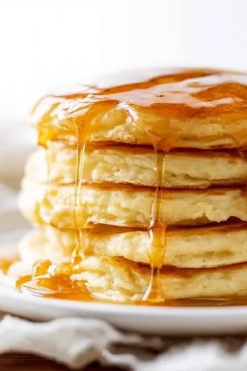 Fluffy sourdough pancakes stacked on a plate with syrup and berries.