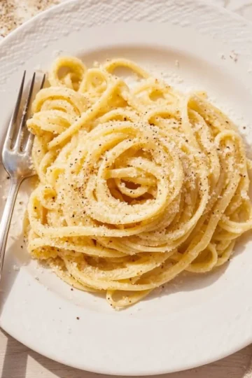 A bowl of cacio e pepe pasta with cheese and black pepper on top.