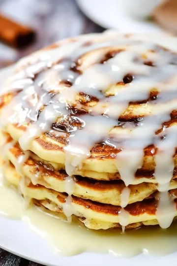 Fluffy cinnamon roll pancakes topped with icing and cinnamon for a delicious breakfast.