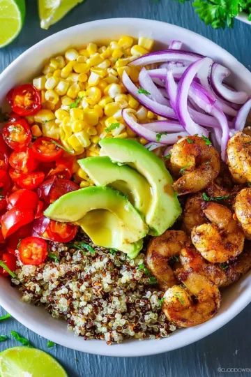 Quinoa bowl with shrimp, vegetables, and herbs on a white plate