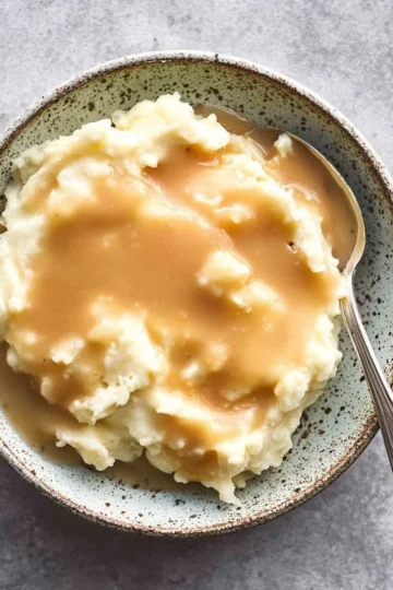 Delicious homemade chicken gravy served over mashed potatoes on a wooden table