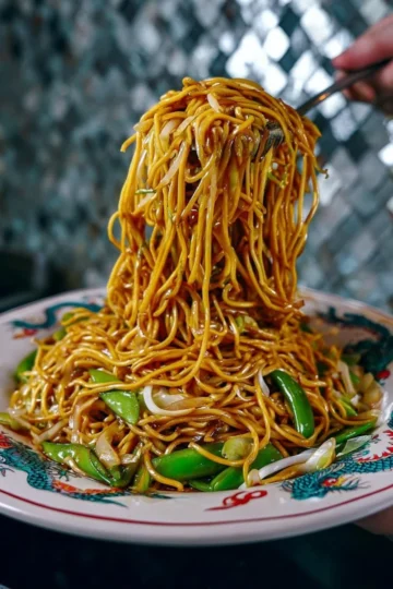 A colorful plate of Lo Mein noodles garnished with vegetables and chicken.