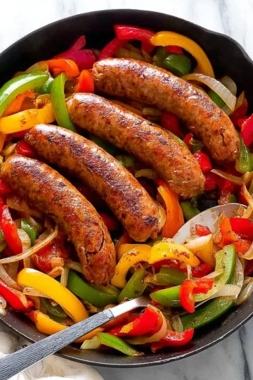 Plate of sausage and peppers served with fresh vegetables and herbs