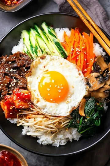 A colorful bowl of bibimbap topped with vegetables, meat, and a fried egg.